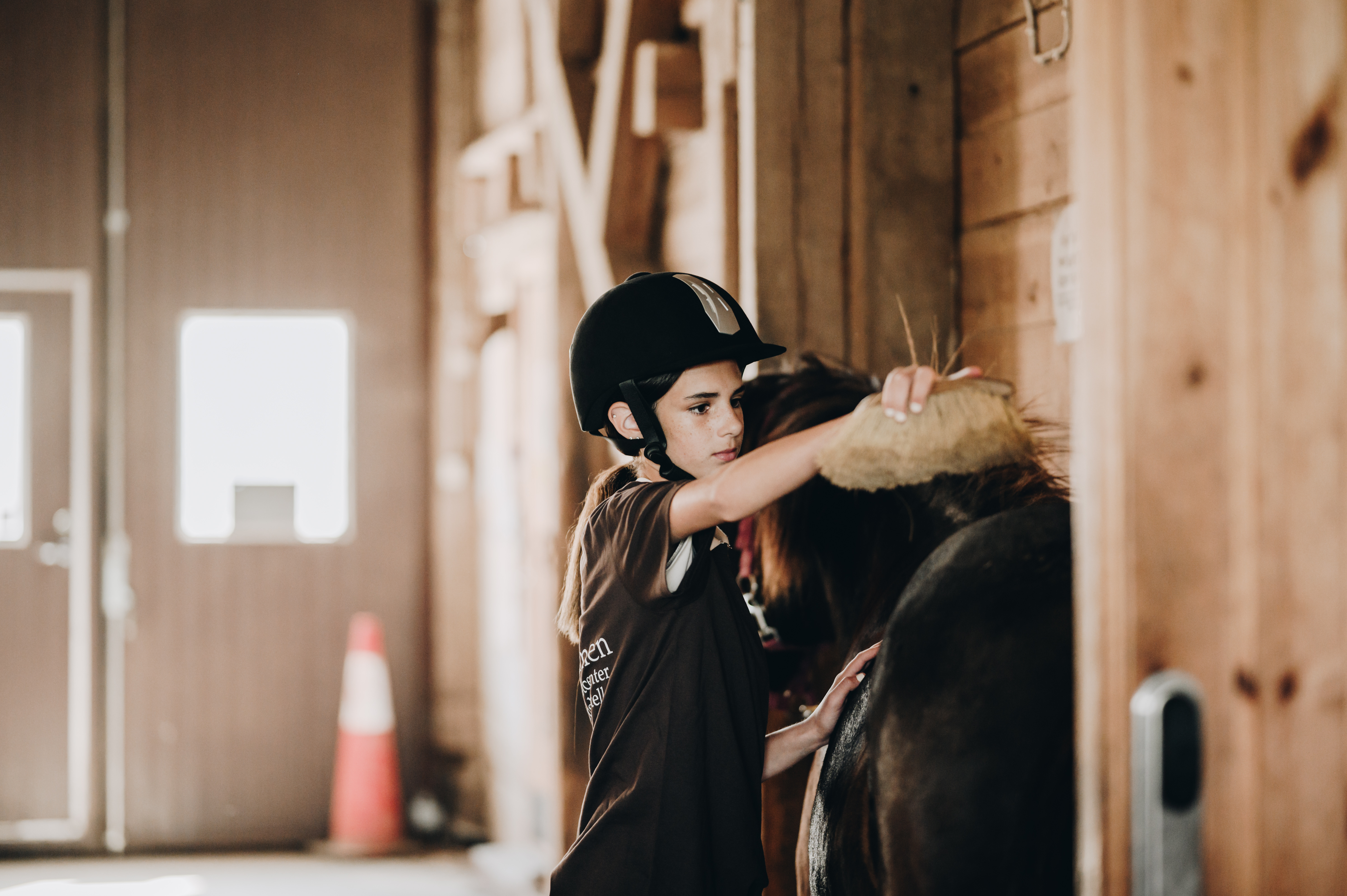 En flicka borstar en häst i ett stall.