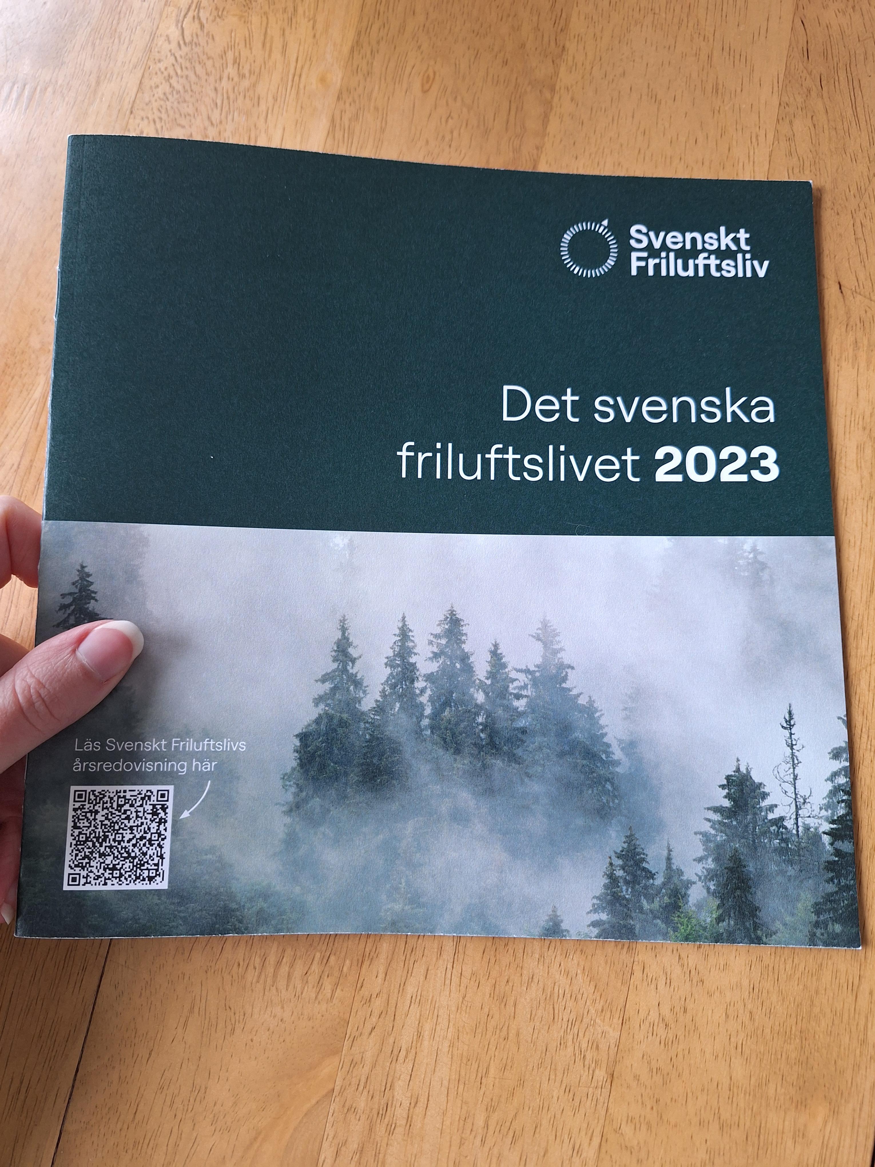 En hand håller i en folder med titeln "Det svenska friluftslivet 2023".